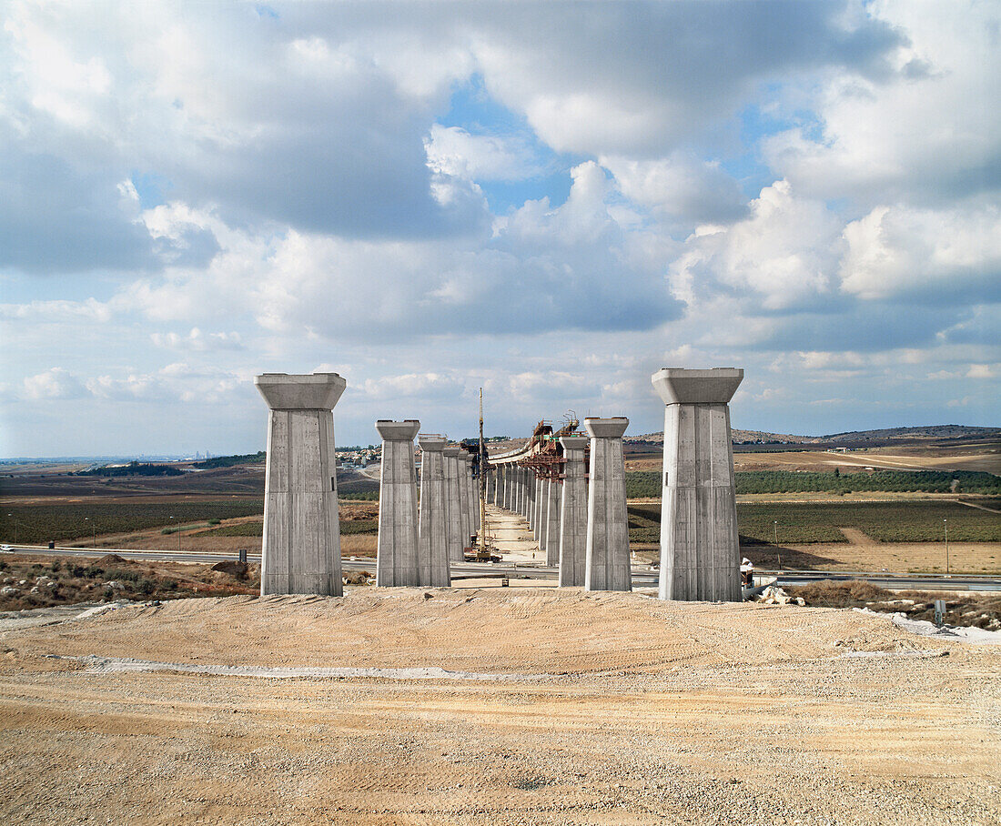 Bridge under construction, pillars and elevated road across an arid landscape, Israel