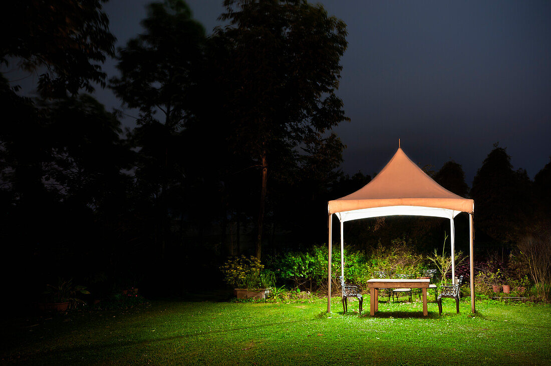 Ein kleiner Pavillon in einem Garten, ein Tisch und eine Sitzgelegenheit und Lichter in der Nacht