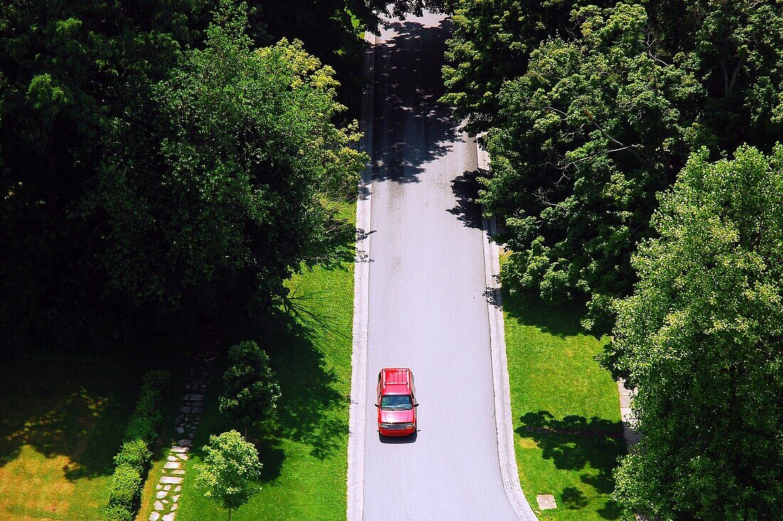 A car makes its way down a country lane in an aerial view.