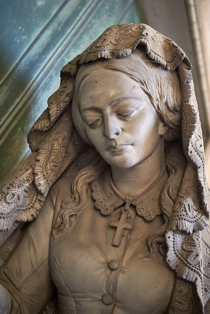 Picture and image of the stone sculpture of a mourning widow who is bringing a crown and knocking on a sepulcher's bronze door,which holds the bas relief of an hourglass,a classic symbol of the passing of time. This theme of the sorrowful survivor in front of the sepulcher's door comes from the Monument dedicated to Maria Christina,Duchess of Teschen,Maria Theresa of Austria's daughter,a neoclassical sculpture. In this version the widow is wearing fashionable clothes,which have been accurately represented,and her openwork shawl. Sculptor G. B. Cevasco 1875. Section A,no 38,The monumental tombs