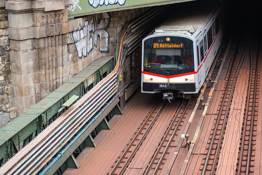 Metro U-Bahn train comes out of a tunnel and goes under Zollamtssteg Bridge while crossing the river in Vienna,Austria.