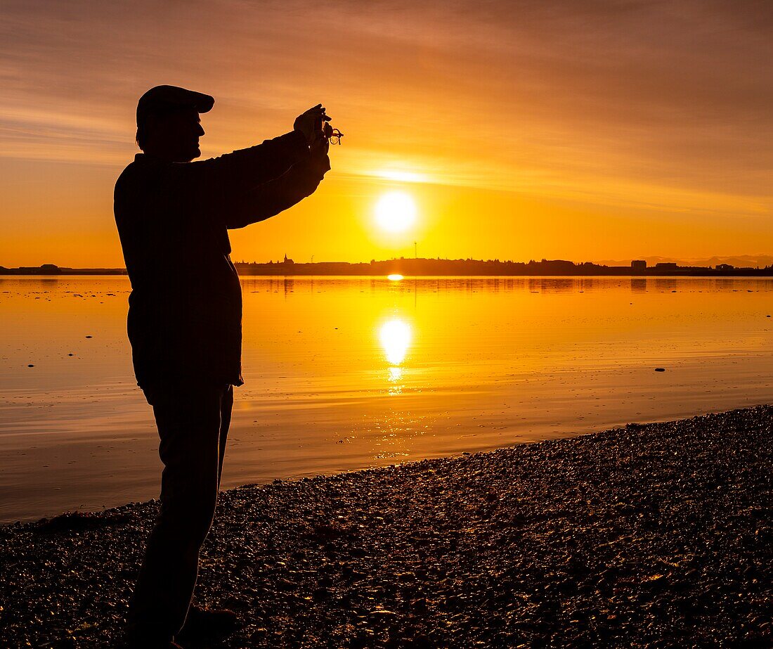 Mann beim Fotografieren bei Sonnenuntergang, Borgarnes, Westisland.