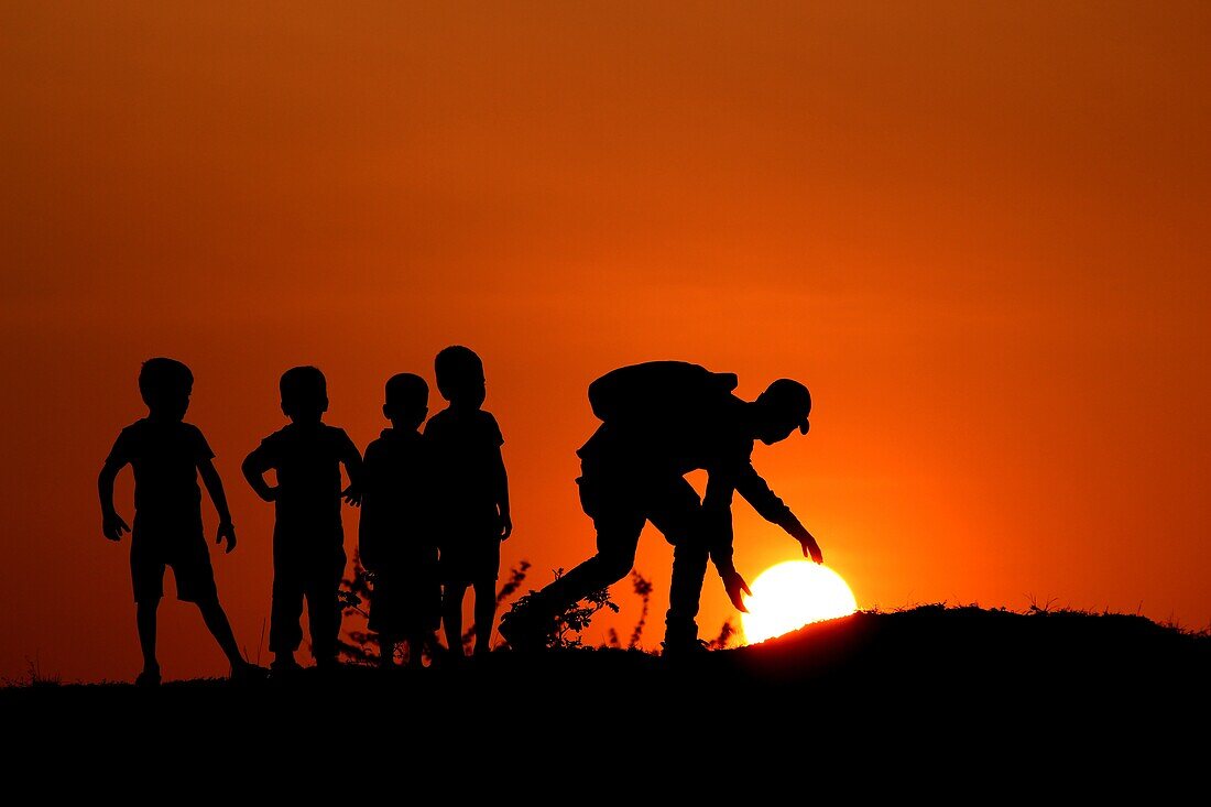 Silhouette of man with the kids touching Sun,Maharashtra,India.