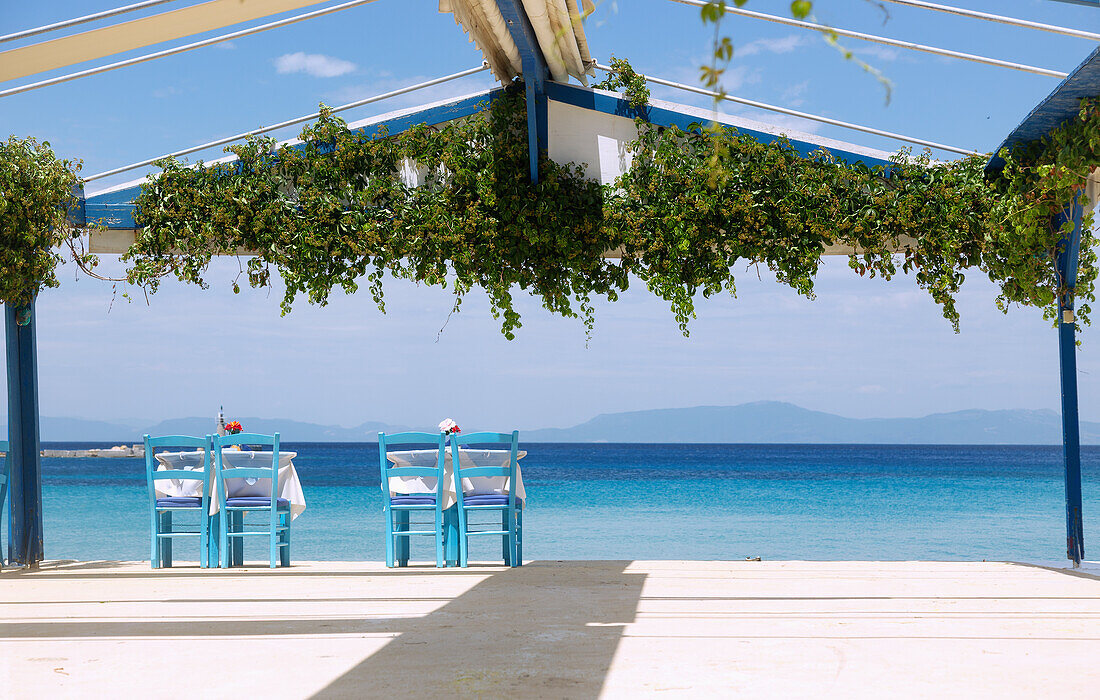 Kokkari, zwei einsame Restauranttische zwischen den Tavernen am Hafen mit Blick aufs Meer auf der Insel Samos in Griechenland