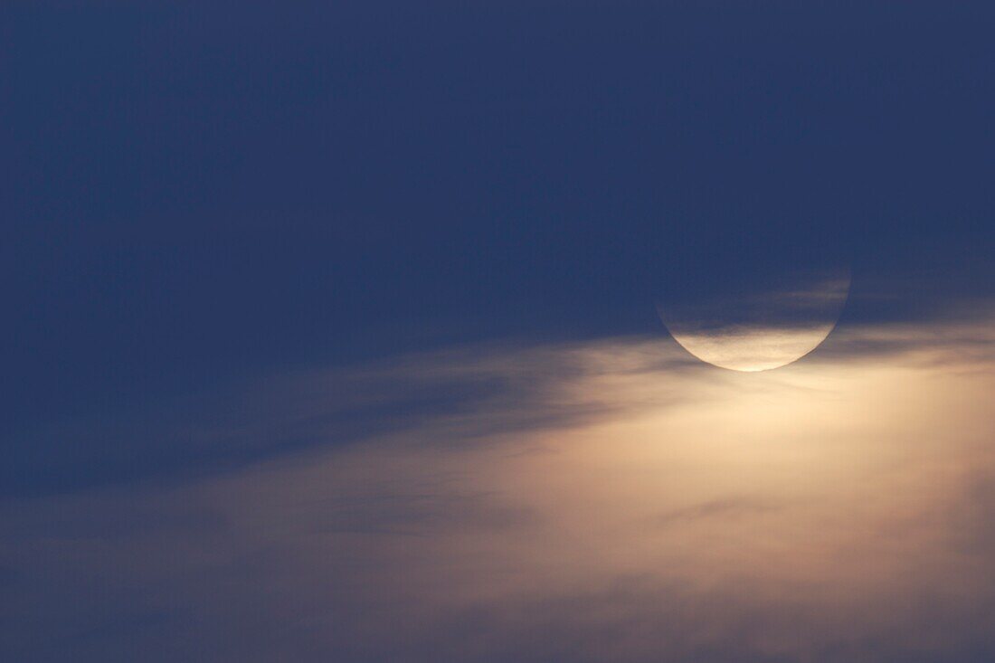 Mondaufgang zur blauen Stunde, in der Dämmerung, teilweise versteckt hinter Hochnebel, Wolken, schöne Stimmung im November.