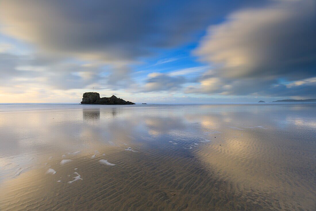 Wolken spiegeln sich im nassen Sand am Strand von Perranporth an der Nordküste von Cornwall, mit Chapel Rock in der Ferne. Das Bild wurde mit Langzeitbelichtung an einem Nachmittag Mitte Februar aufgenommen.