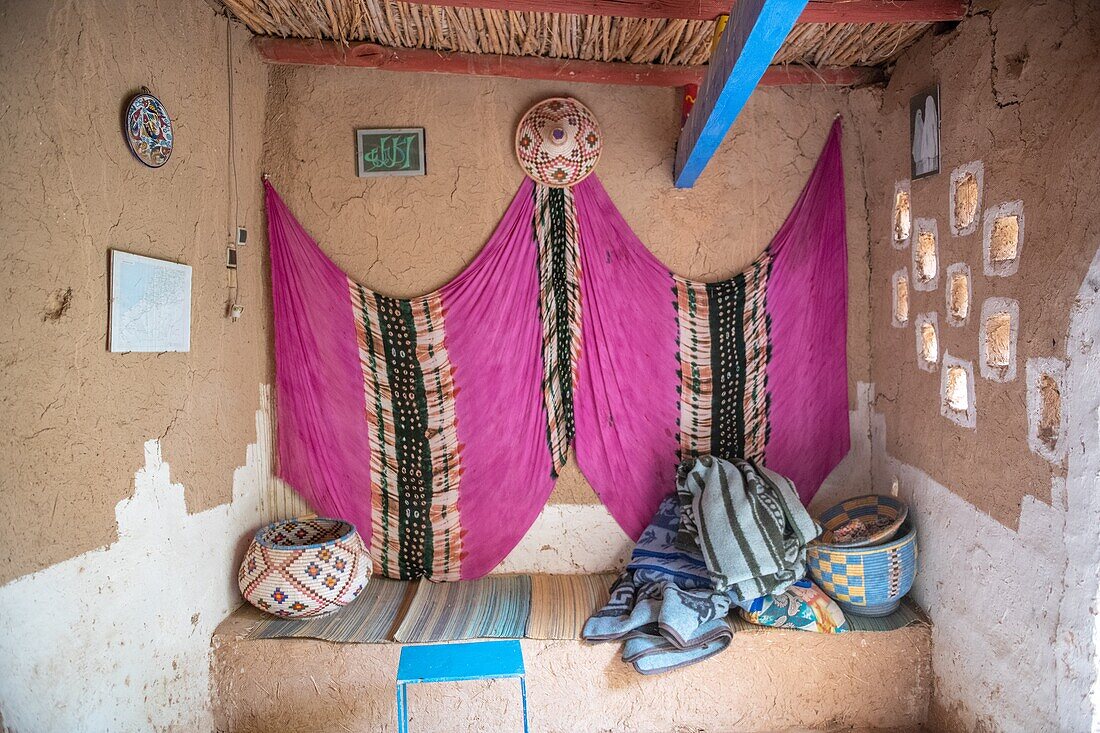Innenraum der Sitzecke mit aufgehängtem buntem Stoff in traditionellem Lehmziegelhaus, Tighmert Oasis, Marokko.