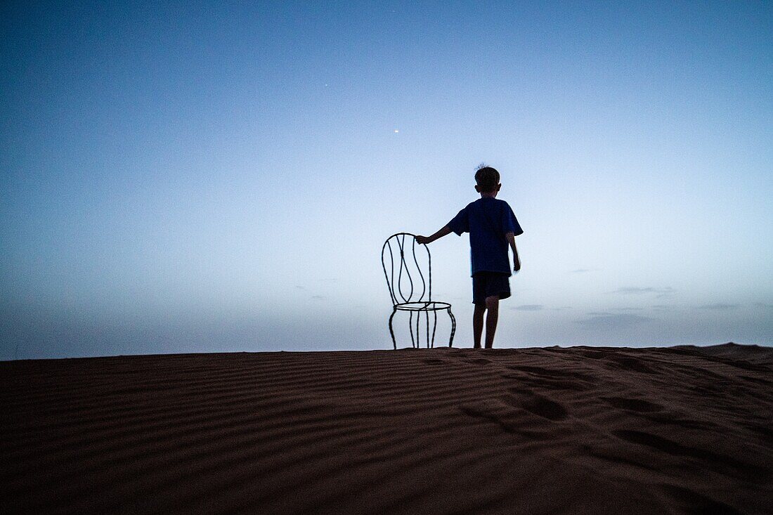 Junge mit Stuhl in der Wüste bei Nacht, Merzouga, Marokko.