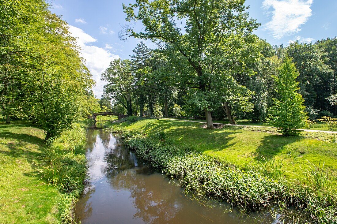 A murky stream is surrounded by use greenery and trees leading to a small bridge at the Museum of Fryderyk Chopin,Polish composer and pianist. Zelazowa Wola,Masovian Voivodeship,Poland.