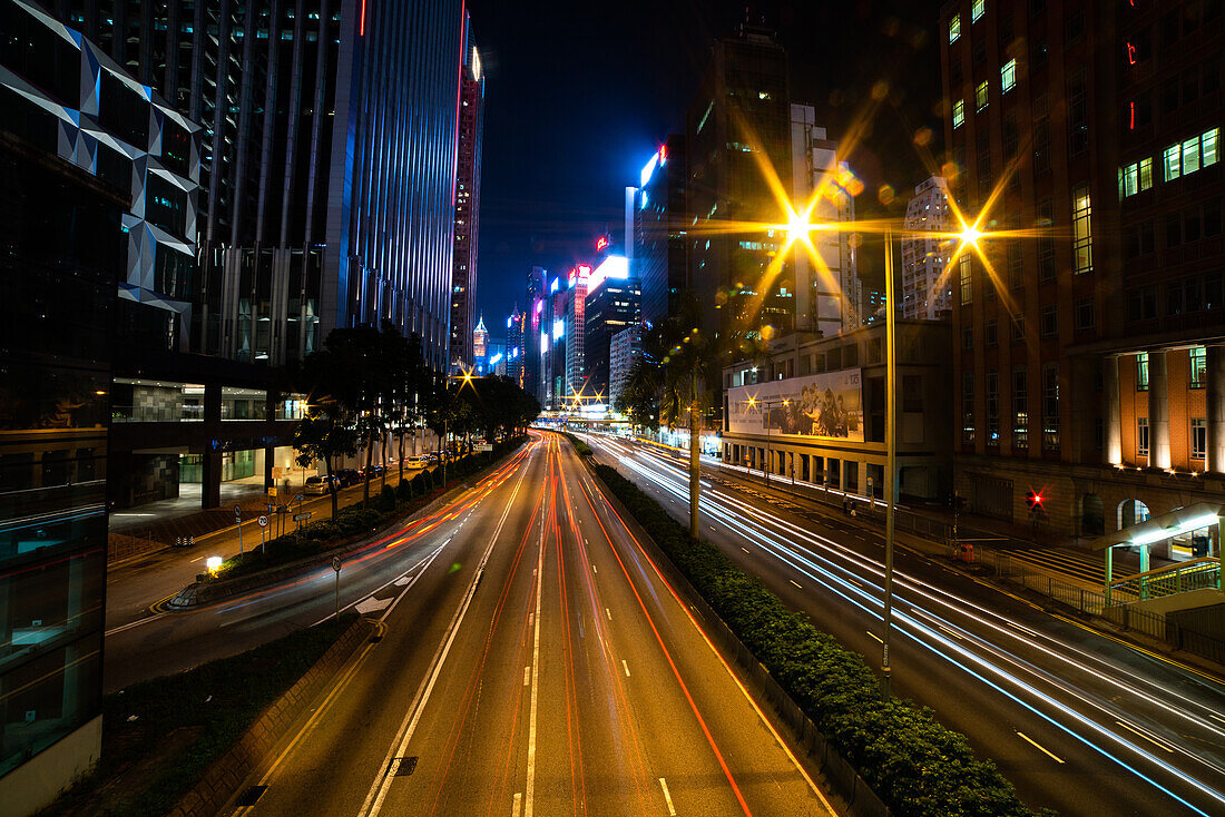 Außenansicht des modernen Stadtbildes mit Langzeitbelichtung von Fahrzeugen, die sich auf der Straße in Hongkong bewegen
