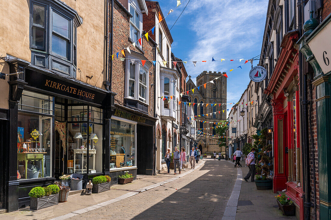 Blick auf Geschäfte und Cafés auf Kirkgate und die Kathedrale im Hintergrund, Ripon, North Yorkshire, England, Vereinigtes Königreich, Europa