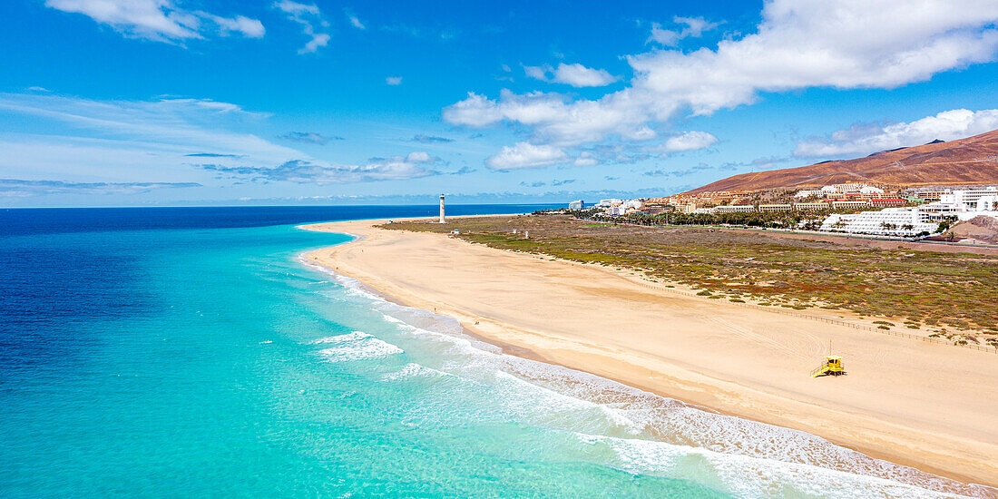 Weißer Sandstrand umspült vom türkisfarbenen Meer mit Leuchtturm im Hintergrund, Morro Jable, Fuerteventura, Kanarische Inseln, Spanien, Atlantik, Europa