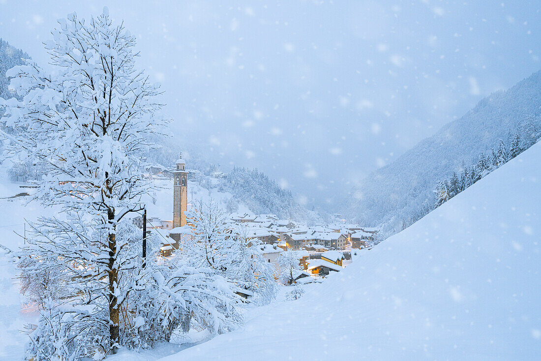 Schneeflocken fallen auf Berghütten im märchenhaften Alpendorf zur Weihnachtszeit, Valgerola, Veltlin, Lombardei, Italien, Europa