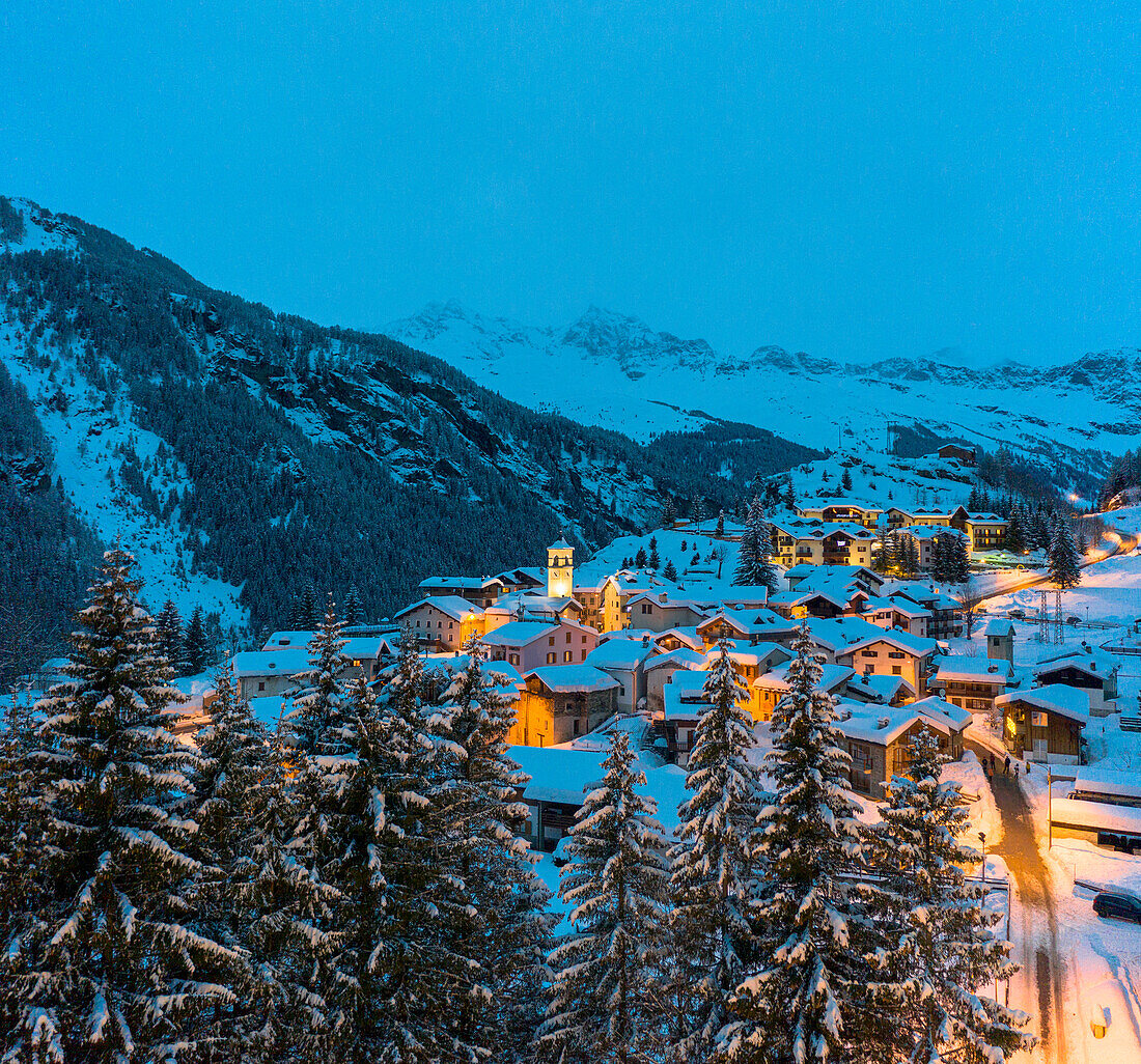 Blaue Dämmerung über schneebedeckten Bergen und Wäldern rund um die Almhütten von Pianazzo, Madesimo, Valle Spluga, Lombardei, Italien, Europa