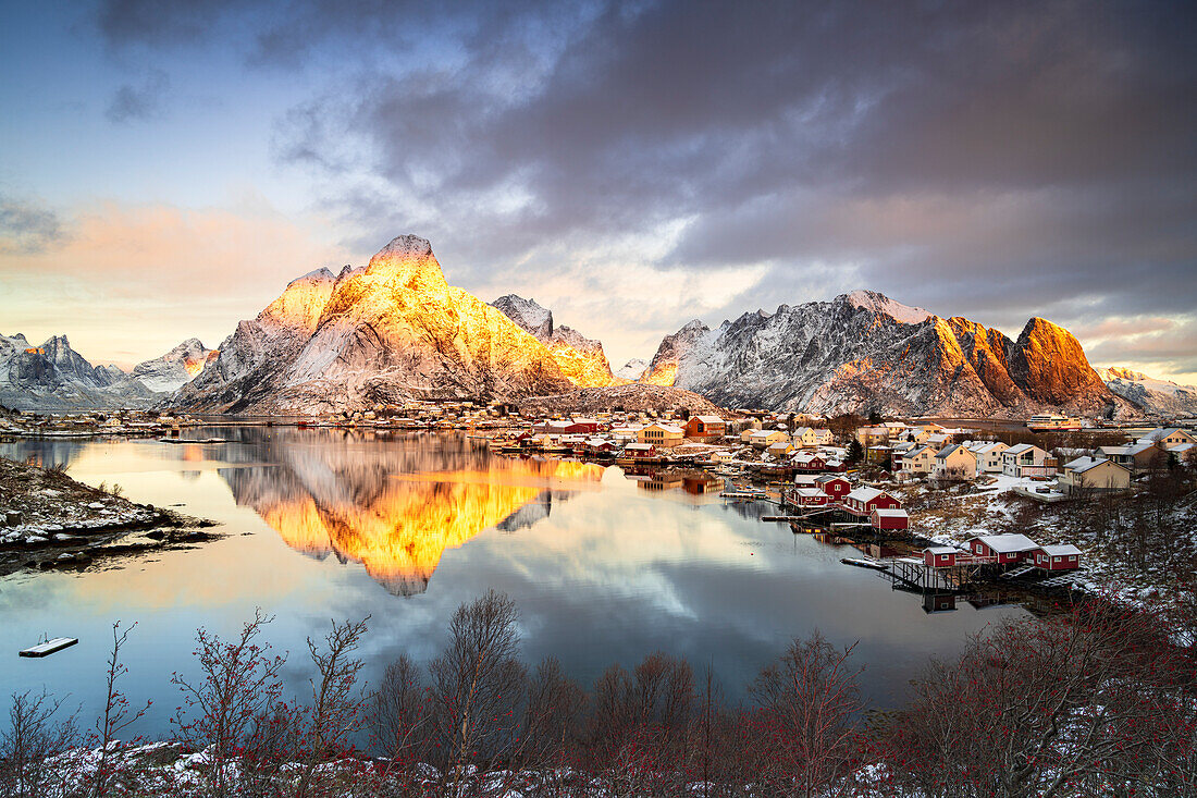 Dramatischer Himmel im Morgengrauen über dem schneebedeckten Berg Olstind, Reine Bay, Nordland, Lofoten-Inseln, Norwegen, Skandinavien, Europa