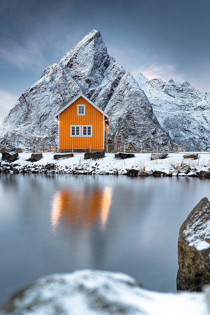 Rorbu im Schnee am Fuße des Olstind-Berges mit Blick auf das Eismeer, Sakrisoy, Reine, Nordland, Lofoten-Inseln, Norwegen, Skandinavien, Europa