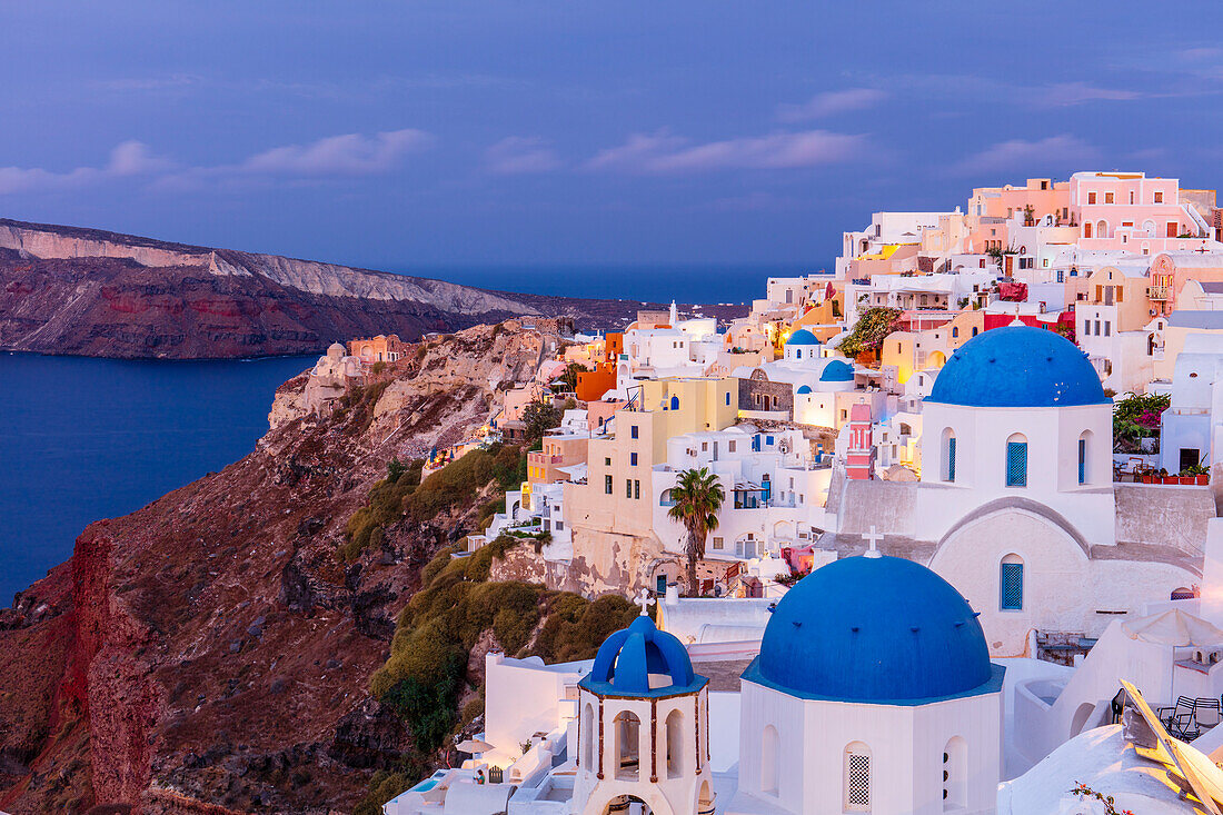 Blaue gewölbte weiße Kirche und bunte Gebäude bei Sonnenaufgang, Oia, Santorini, Kykladen, griechische Inseln, Griechenland, Europa
