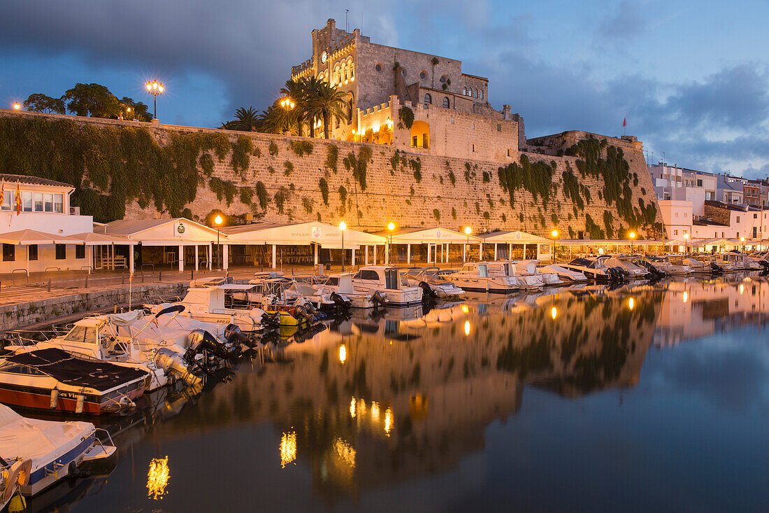 Blick über den ruhigen Hafen zum beleuchteten Rathaus in der Abenddämmerung, Ciutadella (Ciudadela), Menorca, Balearen, Spanien, Mittelmeer, Europa
