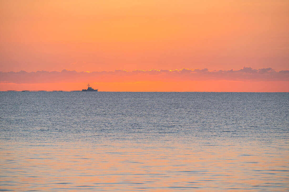 Ruhiges Meer bei Sonnenaufgang mit Fischerboot in der Ferne