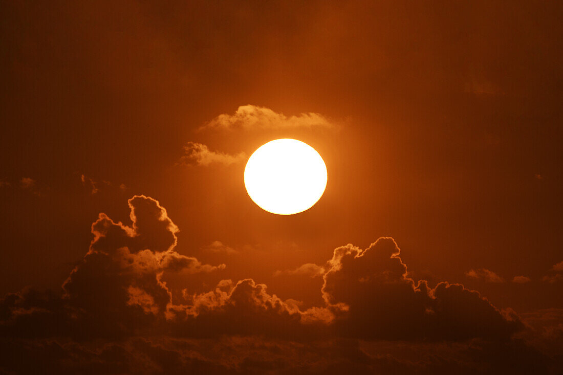 Helle Sonne bei Sonnenuntergang mit Wolken gegen orangefarbenen Himmel