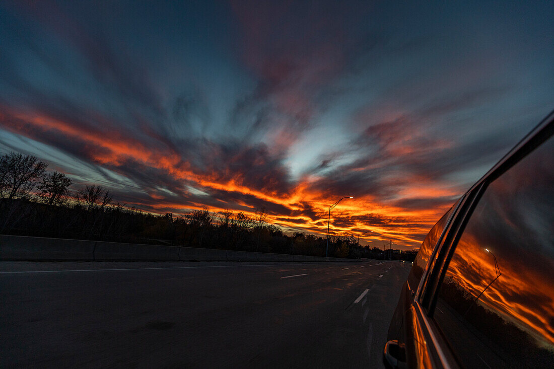 USA, Idaho, Boise, Sonnenuntergang spiegelt sich im Seitenfenster des Autos, das auf der Autobahn fährt