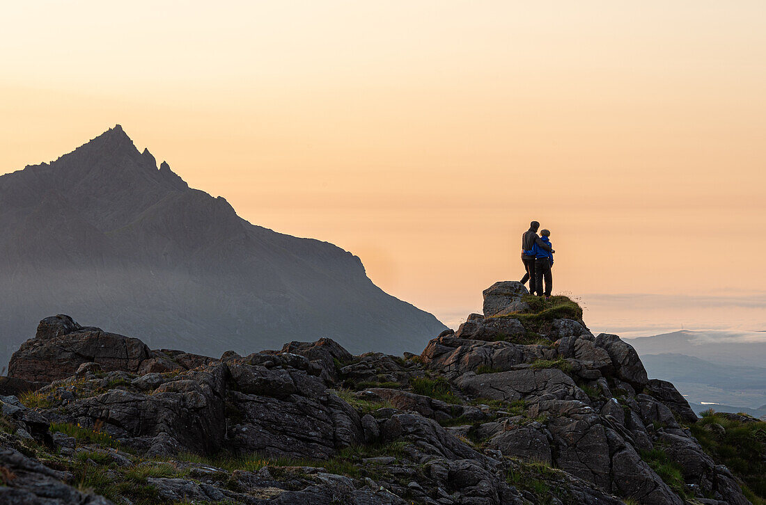 Ein Paar steht auf einem felsigen Gipfel und beobachtet einen Bergsonnenuntergang mit Sgurr nan Gillean im Hintergrund, Isle of Skye, Innere Hebriden, Schottland, Vereinigtes Königreich, Europa