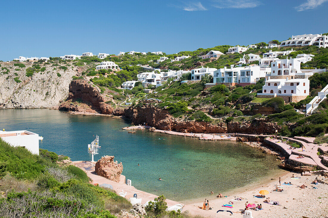 Blick über den Sandstrand zum Wohnhang oberhalb der Bucht mit klarem türkisfarbenem Wasser, Cala Morell, Menorca, Balearen, Spanien, Mittelmeer, Europa