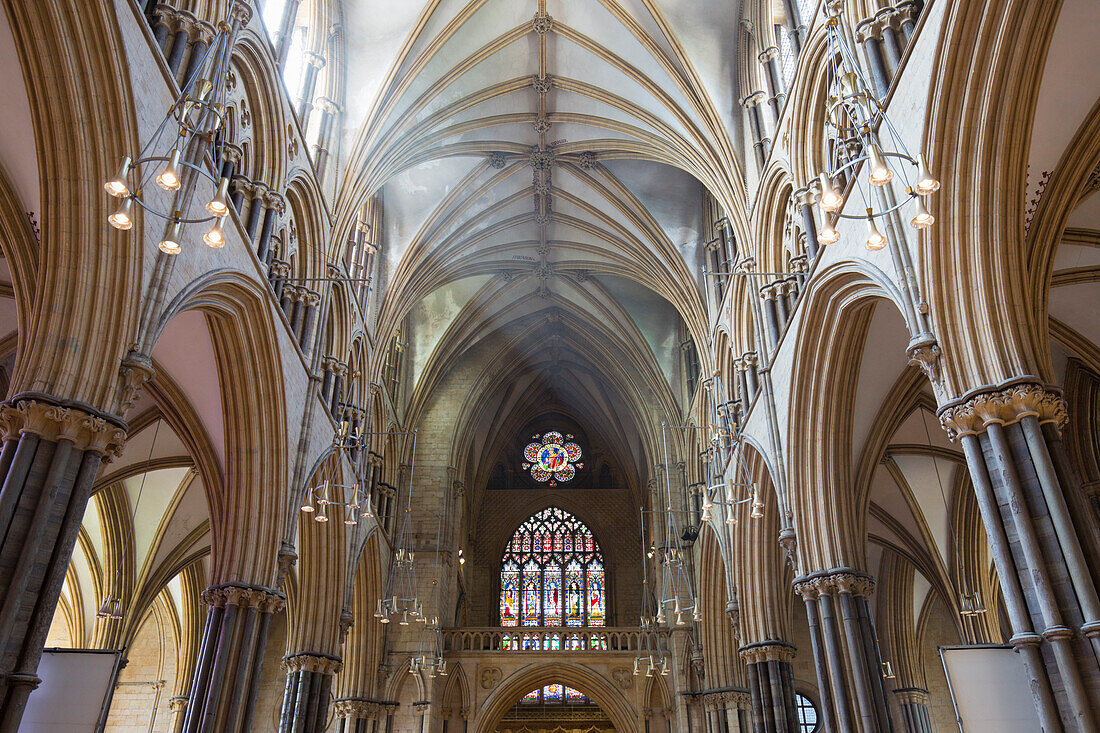 Blick entlang des sonnendurchfluteten Kirchenschiffs auf das bunte Glasfenster Great West der Kathedrale von Lincoln, Lincoln, Lincolnshire, England, Vereinigtes Königreich, Europa