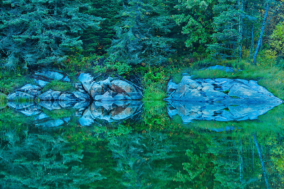 Kanada, Ontario, Distrikt Kenora. Wald und Ufer spiegeln bei Sonnenuntergang den Middle Lake wider