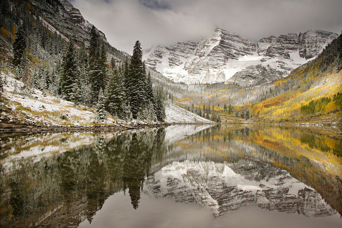 USA, Colorado, White River National Forest, Morning light on Maroon Bells peaks reflects fresh snow and autumn color on Maroon Lake