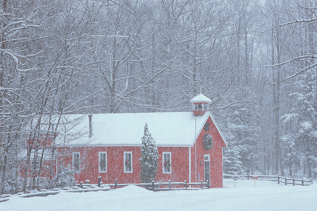 USA, Michigan, altes rotes Schulhaus und Wald im Schneefall zur Weihnachtszeit