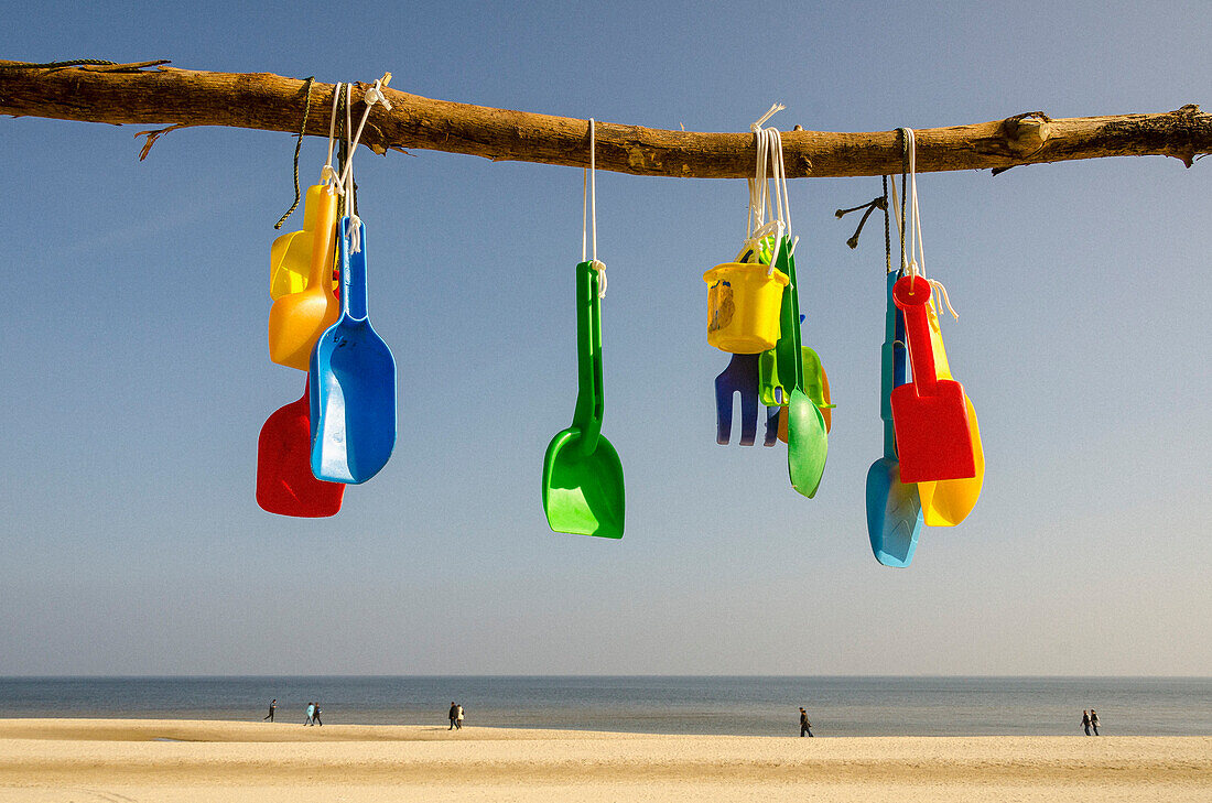 Bunte Plastikschaufeln, die am sonnigen Strandzweig hängen