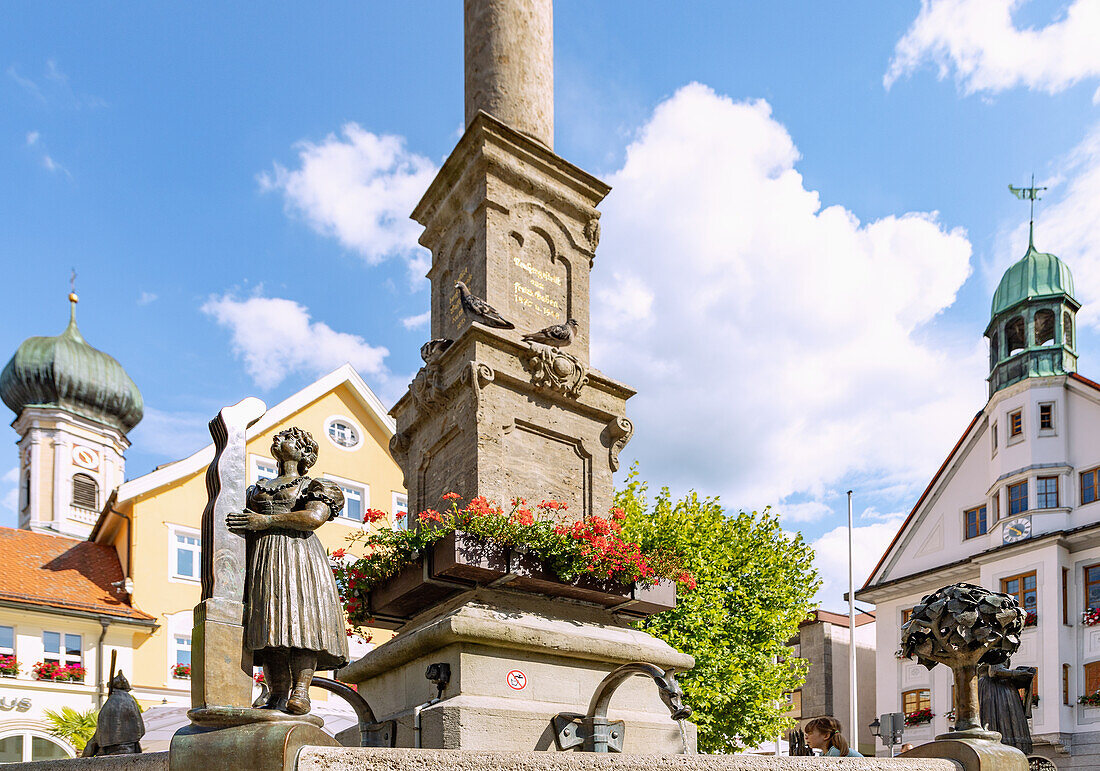 Fountain with bronze figure of the stocking shaper and Marian column at Marienplatz with parish church of St. Nicholas and town hall in Immenstadt im Allgäu in Bavaria in Germany