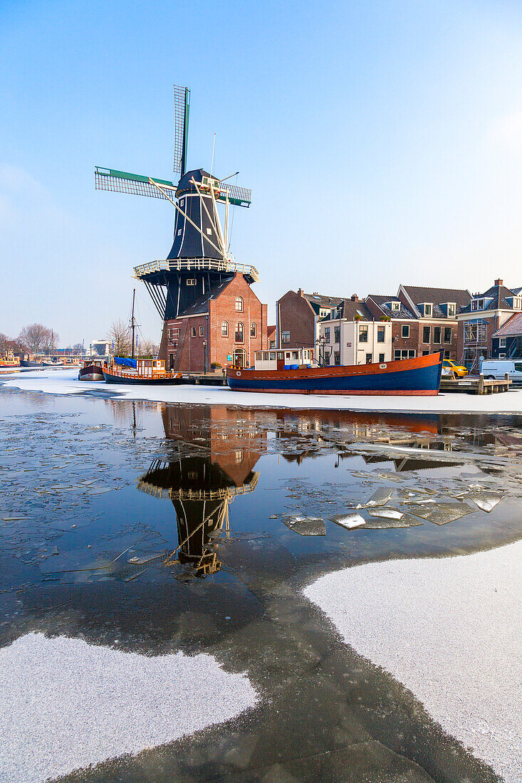 Windmühle De Adriaan spiegelt sich im Kanal des eisigen Flusses Spaarne, Haarlem, Amsterdam, Nordholland, Niederlande, Europa
