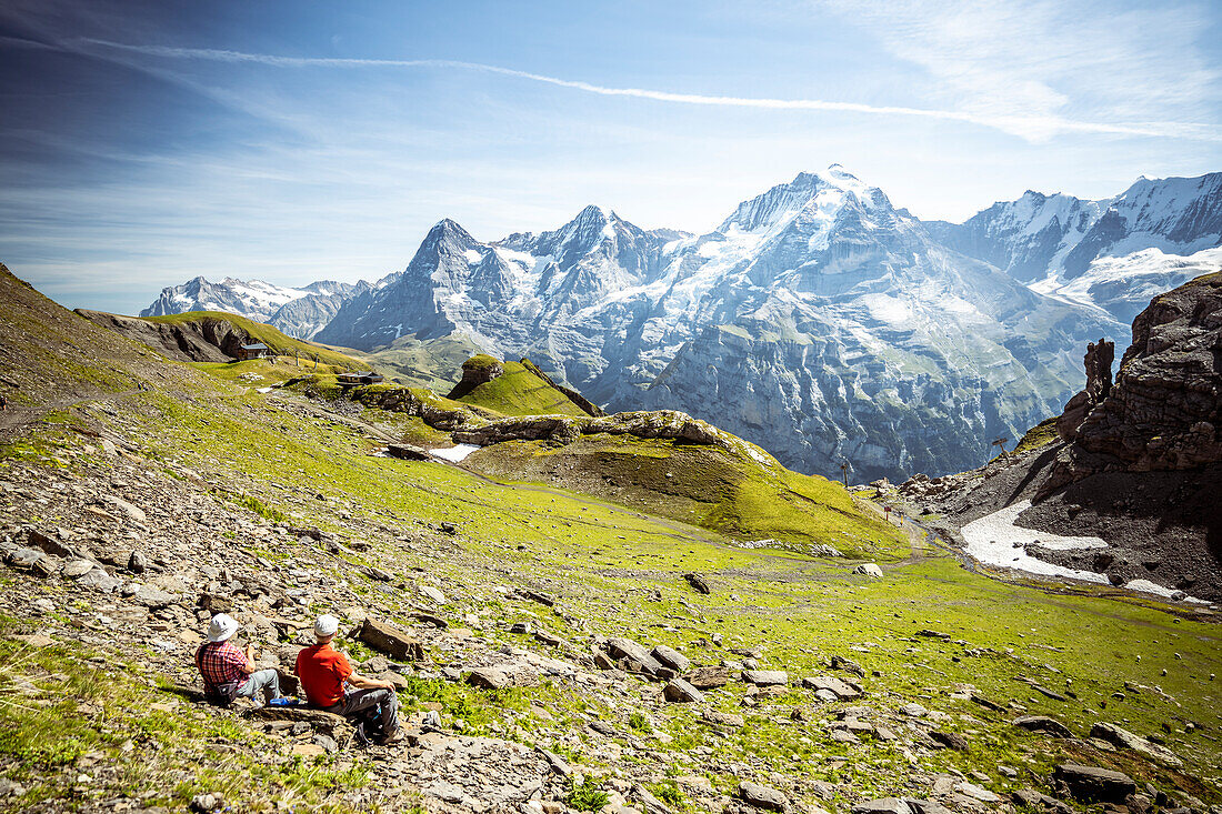 Two people admiring Eiger, Monch and Jungfrau mountains from meadows, Murren Birg, Jungfrau Region, Bern Canton, Swiss Alps, Switzerland, Europe