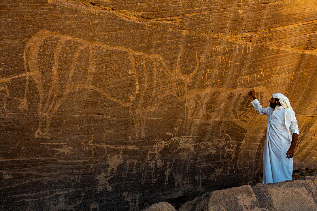 Man pointing at rock carvings, Bir Hima Rock Petroglyphs and Inscriptions, UNESCO World Heritage Site, Najran, Kingdom of Saudi Arabia, Middle East