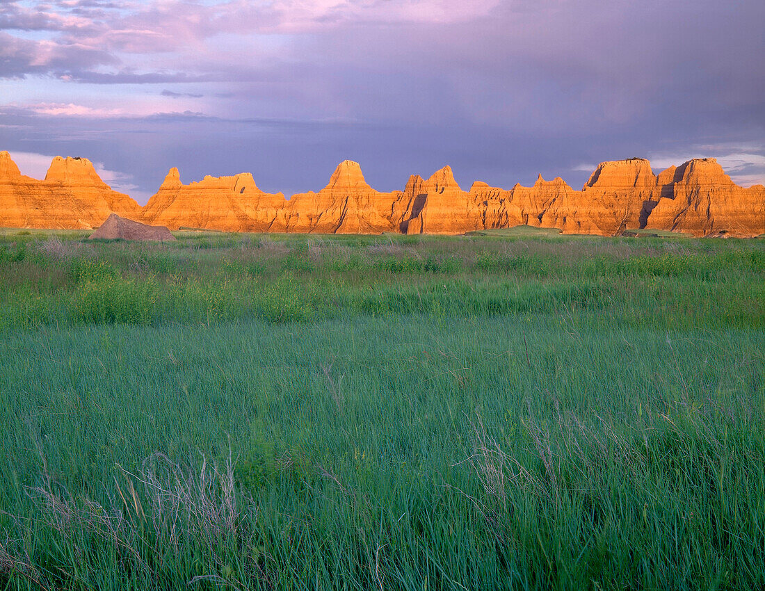 USA, South Dakota, Badlands National Park, Sonnenaufgangslicht auf erodierten Zinnen über frühlingsgrünen Präriegräsern, in der Nähe von Castle Trail, North Unit.
