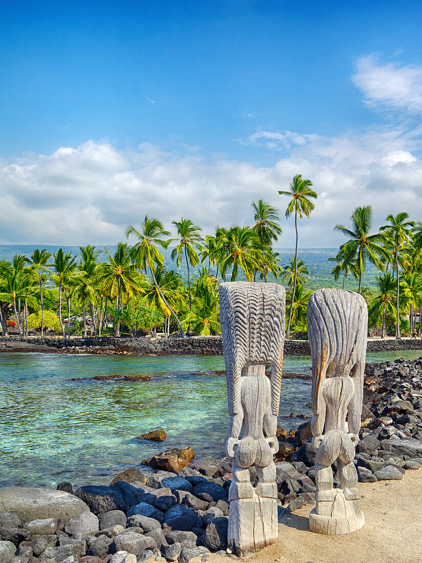 USA, Hawaii, Big Island. Palm trees and ancient tiki wooden carvings at the National Historic Park Pu'uhonua o Honaunau.