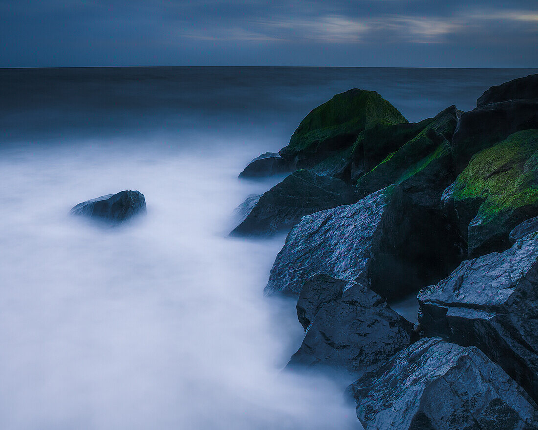 USA, New Jersey, Cape May National Seashore. Wellen, die sich bei Sonnenuntergang an Felsen brechen.