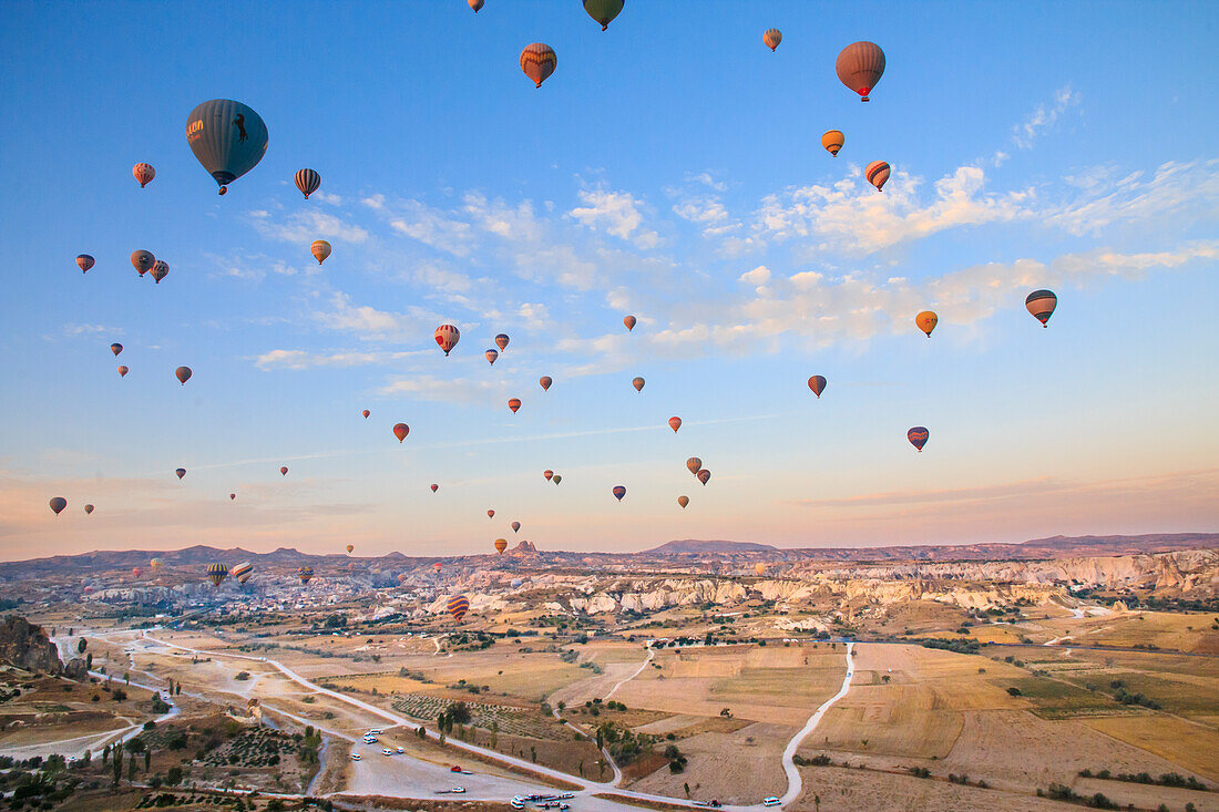 Türkei, Anatolien, Kappadokien, Goreme. Heißluftballons fliegen über Felsformationen und Feldlandschaften im Red Valley, Goreme-Nationalpark, UNESCO-Welterbestätte.