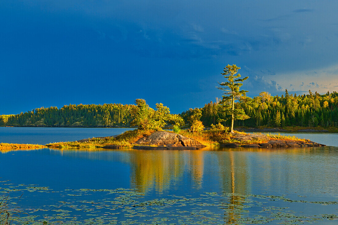 Kanada, Ontario, Distrikt Kenora. Herbstfarben des Waldes spiegeln sich bei Sonnenuntergang auf dem Middle Lake wider