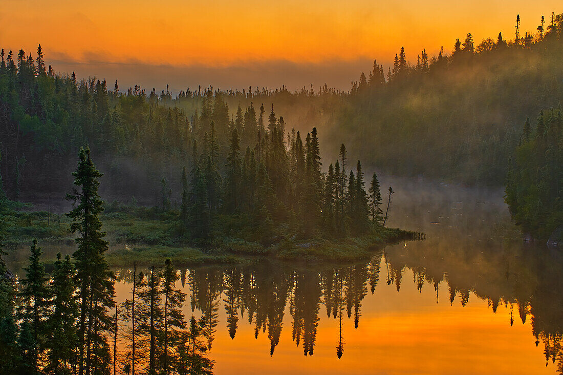 Canada, Ontario, Schreiber. Sunrise fog and forest reflect in lake.