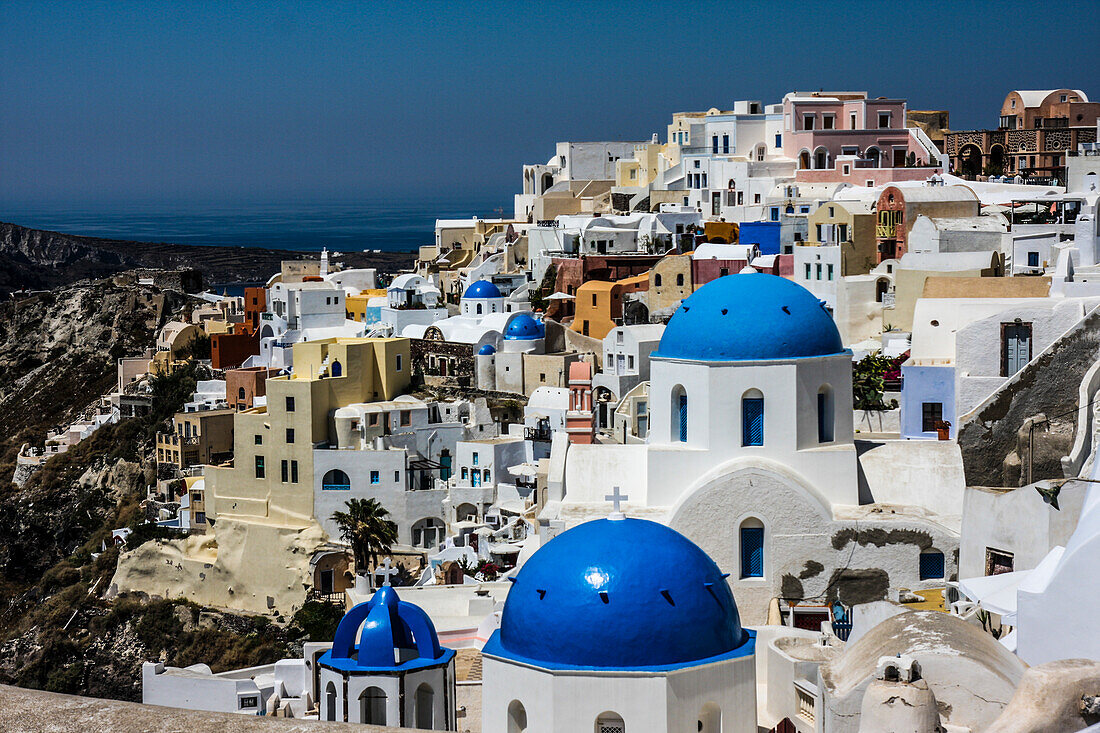 Oia, Santorini, Greece. Blue dome Greek Orthodox churches, white washed and colored buildings over looking the Aegean Sea