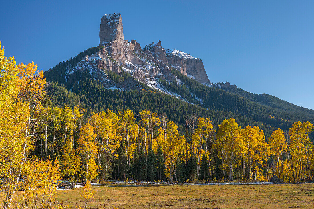 USA, Colorado. Uncompahgre National Forest, Chimney Rock (links) und Courthouse Mountain (rechts) über Wiese und herbstfarbenem Wald.