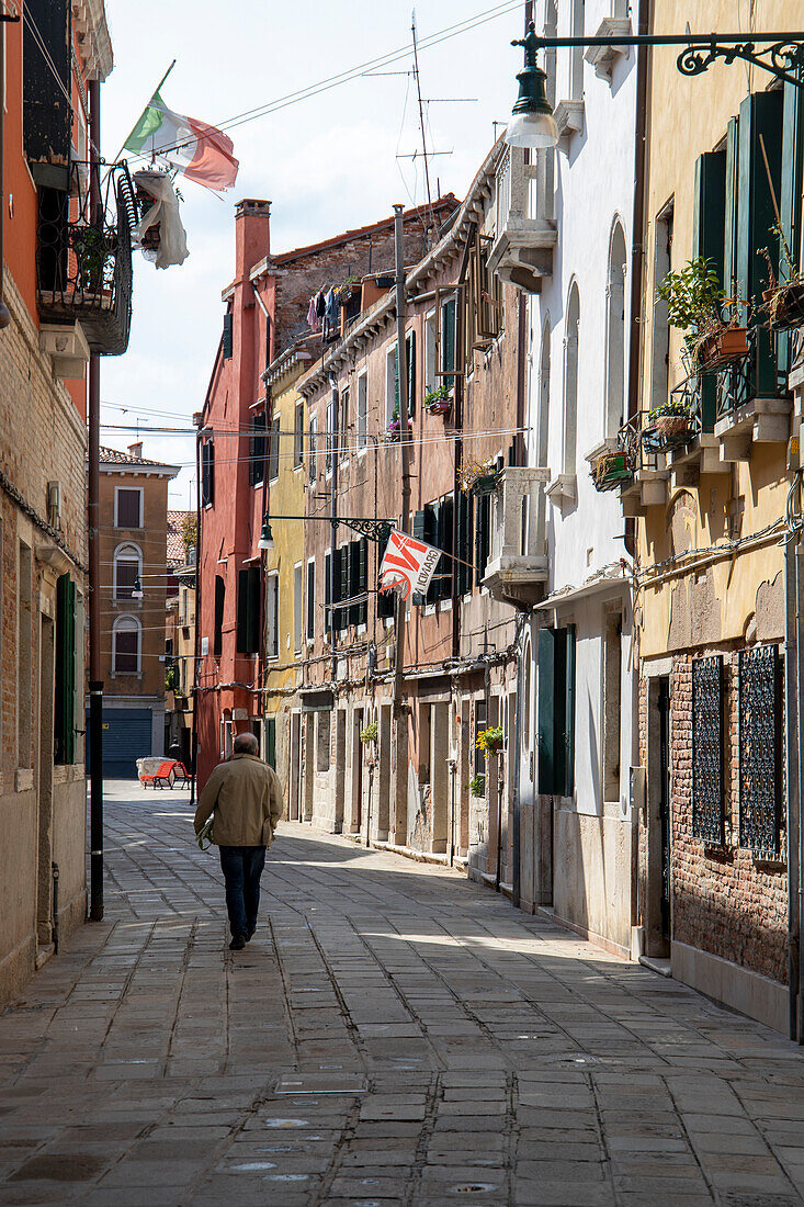 A lonely man walks along a narrow street in the shade of the houses, Venice, Veneto, Italy