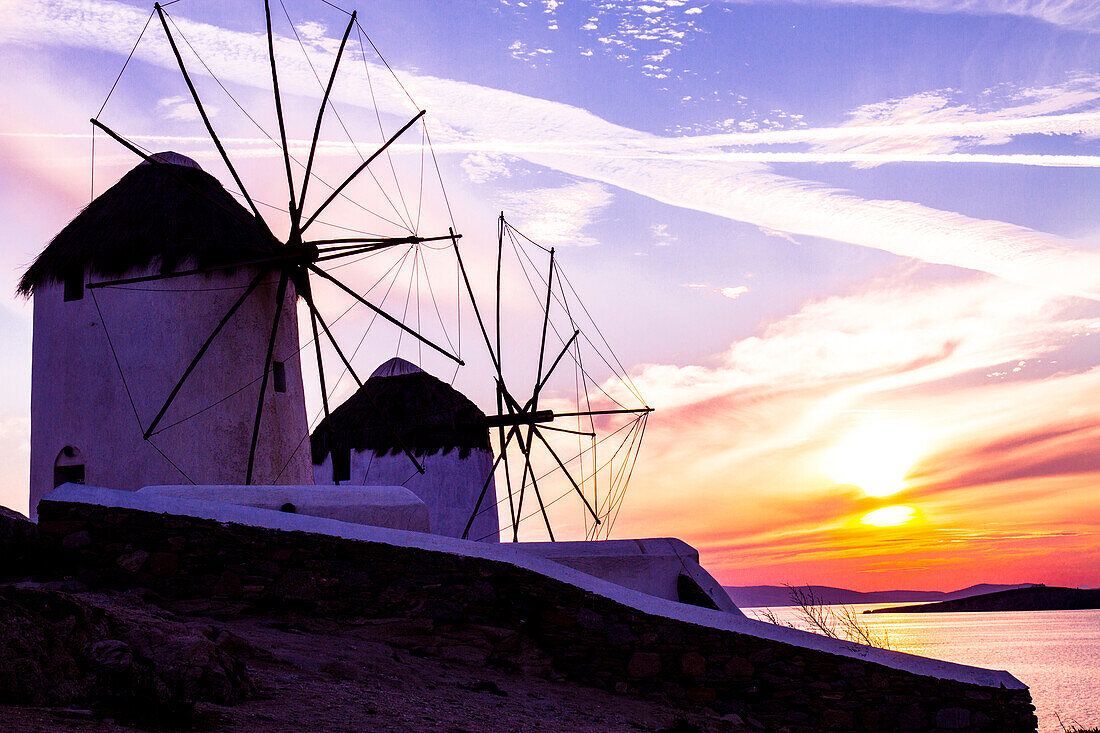 Mykonos, Griechenland. Zwei Windmühlen mit einem goldenen, rosa und blauen Sonnenuntergang auf dem Ägäischen Meer