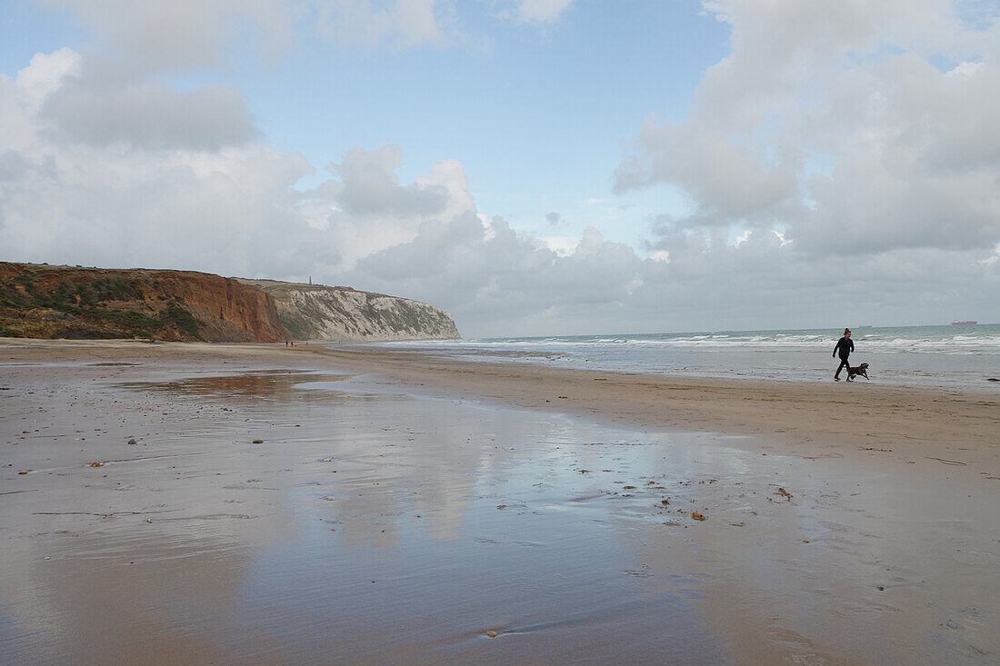 Frau mit Hund bei einem Strandspaziergang am Yaverland Beach auf der Isle of Wight mit Kreidefelsen im Hintergrund, Südengland, England, Großbritannien, Europa