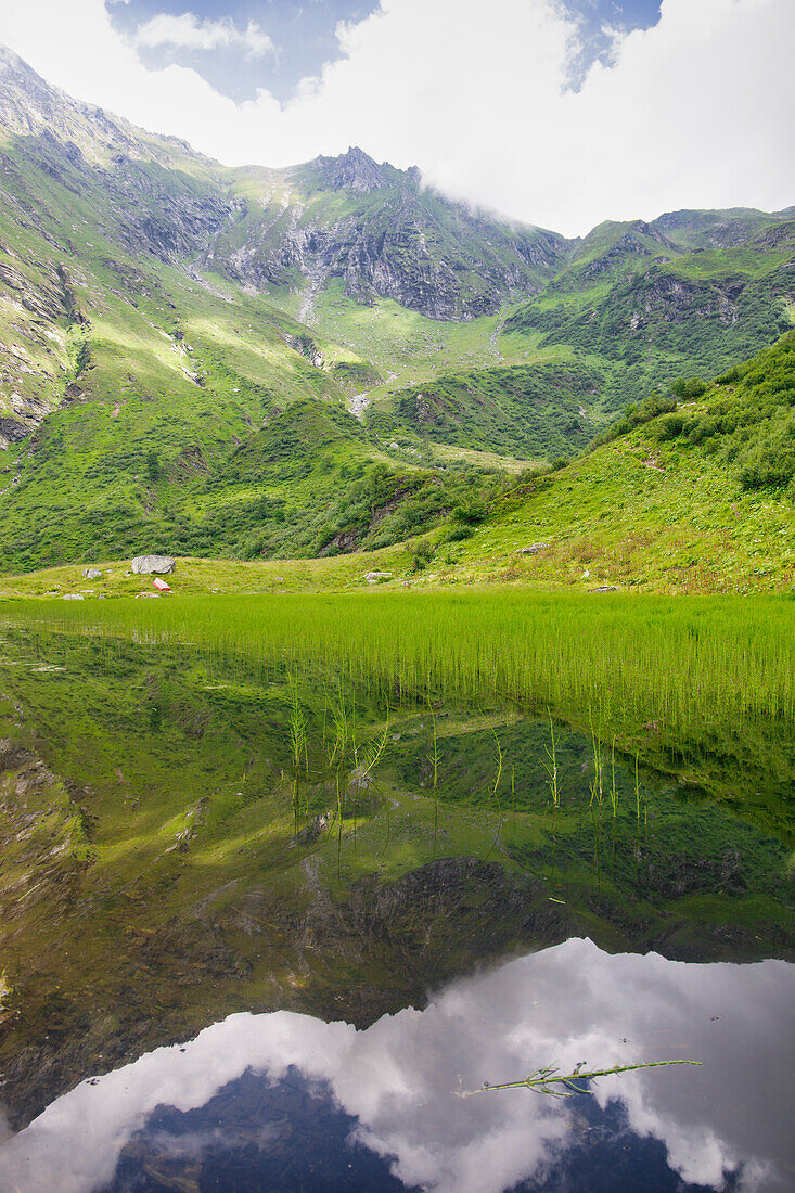 Die Berge des Valsesia spiegeln sich in einem kleinen Bergsee. Alpe Campo, Piemont, Italien.