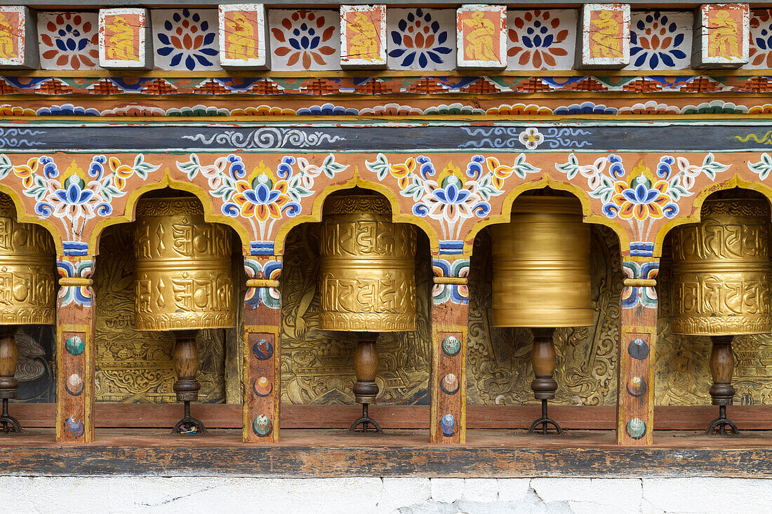 Bhutan. Sich drehende Gebetsmühlen entlang einer Tempelmauer.
