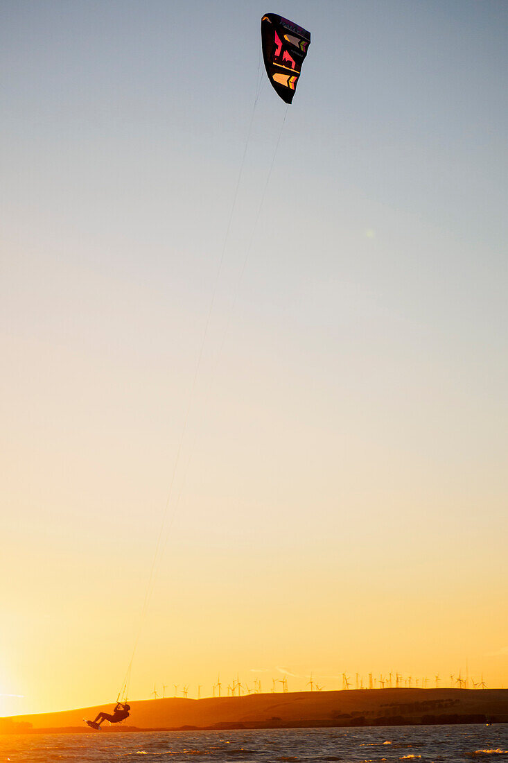 USA, Kalifornien, Rio Vista, Sacramento River Delta. Kiteboarder, der bei Sonnenuntergang Luft holt.